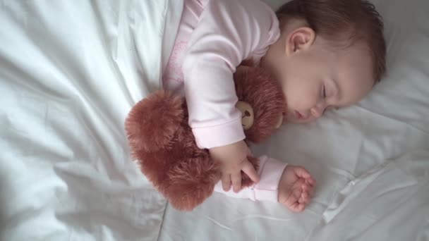 Auténtico retrato lindo bebé caucásico regordete niña o niño en sueño rosa con oso de peluche en la cama blanca. niño descansando a la hora del almuerzo. cuidado, Niñez durmiente, Infancia, paternidad, concepto de vida — Vídeo de stock