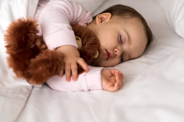 Αυθεντικό πορτρέτο χαριτωμένο καυκάσιο μικρό παχουλό κοριτσάκι ή αγόρι σε ροζ ύπνο με αρκουδάκι στο λευκό κρεβάτι. το παιδί ξεκουράζεται το μεσημέρι. φροντίδα, Υπνηλία, Παιδική ηλικία, Parenthood, έννοια της ζωής — Φωτογραφία Αρχείου