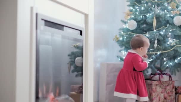 Authentique Joie mignonne et joyeuse petite fille joufflue portant un chapeau de Père Noël et une robe rouge sourire jouer avoir du plaisir à célébrer le nouvel an ambiance festive près de l'arbre de Noël à la maison. Enfance, hollyday, concept d'hiver — Video