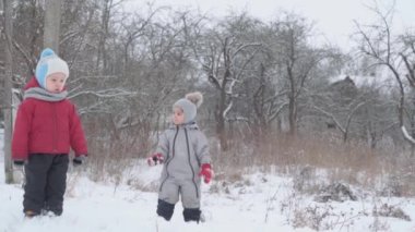 Tatil, oyun, aile kavramı - yavaş çekim otantik iki mutlu anaokulu çocuğu kardeş tepeden aşağı kayıp birbirlerine tırmanmada yardım ediyorlar. Soğuk mevsimde kar yağışı, kış parkında açık havada.