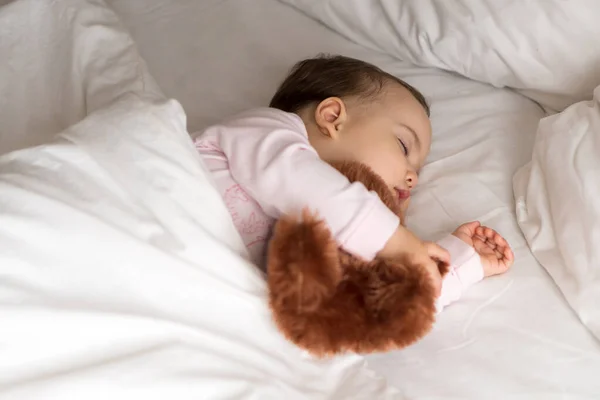 Authentiek portret schattig Kaukasisch klein baby mollig meisje of jongen in roze slaap met teddybeer op wit bed. kind rust uit rond lunchtijd. verzorging, Slaapkind, Jeugd, Ouderschap, levensloop — Stockfoto