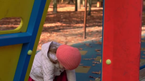 Childhood, family, motherhood, Activities concept - preschool minor child boy girl 2-4 years in red orange beret playing on playground in autumn park. small kid have fun on slides and arcades outdoors — Stock Video