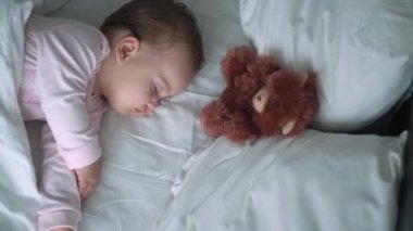 Otantik portre, beyaz yatakta oyuncak ayıyla pembe uykuda olan beyaz, beyaz, küçük, beyaz, tombul bir bebek bebek ya da oğlan. Çocuk öğle yemeği vakti dinleniyor. Bakım, Uyuyan Çocuk, Çocukluk, Ebeveynlik, Hayat Konsepti