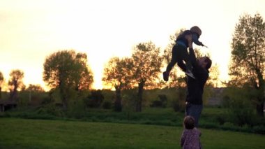 Parktaki insanlar. Gün batımında mutlu aile silueti. Babasının çocuğu havaya atması çok zaman aldı. Aileler ve eğlenceli çocuklar açık havada yürüyorlar. Babalar Günü, çocukluk, ebeveynlik kavramı.