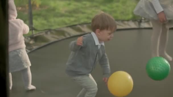 Primavera, deporte, día de fiesta, familia, infancia - cámara lenta Tres hermanos preescolares niños pequeños felices niños gemelos jugar divertirse saltar bolas en trampolín al aire libre soleado atardecer en el parque — Vídeo de stock