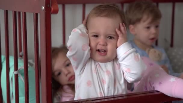 Lindo alegre 3 niños pequeños niña y hermanos varones niños preescolares en cuna de bebé gris después de despertar de dormir en pijama con las piernas colgando. Infancia, ocio, comodidad, medicina, concepto de salud — Vídeo de stock