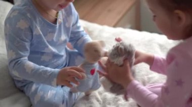 İki tane gülümseyen anaokulu çocuğu erkek ve kız çocuğu yatakta mavi pijamalı oyuncak ayıyla oynuyorlar. Küçük bebek ikizler evde karantinada mutlu çocuklar. Arkadaşlık, aile, eğitim kavramı