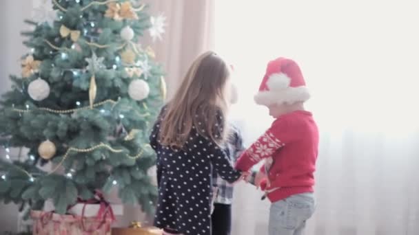 3 niños felices auténticos de la alegría alrededor de la danza cogidos de la mano caminan en círculo por el juego del árbol de Navidad se divierten juntos. Los niños preescolares celebran el ambiente festivo de Año Nuevo. Invierno, concepto de vacaciones — Vídeos de Stock