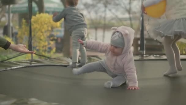 Vår, sport, høytid, familie, barndom, langsom bevegelse Tre glade små barn førskolebarn Barn leker morsomme hoppeballer på trampoline utenfor solnedgang i parken – stockvideo