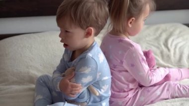 İki tane gülümseyen anaokulu çocuğu erkek ve kız çocuğu yatakta mavi pijamalı oyuncak ayıyla oynuyorlar. Küçük bebek ikizler evde karantinada mutlu çocuklar. Arkadaşlık, aile, eğitim kavramı
