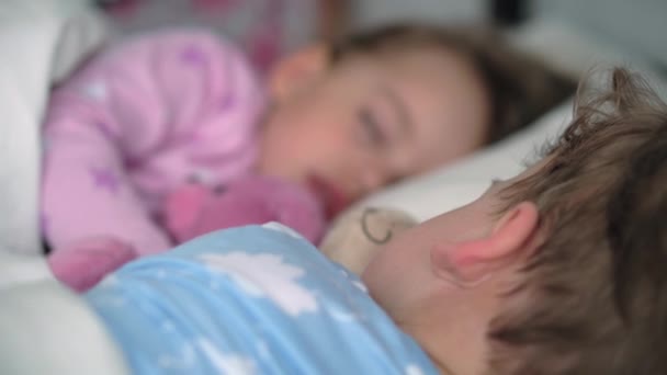 Autentický portrét roztomilé kavkazské malé předškolní sourozence chlapeček a dívka v modrém růžovém pyžamu spát s medvídkem na bílé posteli. dětský odpočinek, péče, medicína a zdraví, Dětství, životní koncept — Stock video