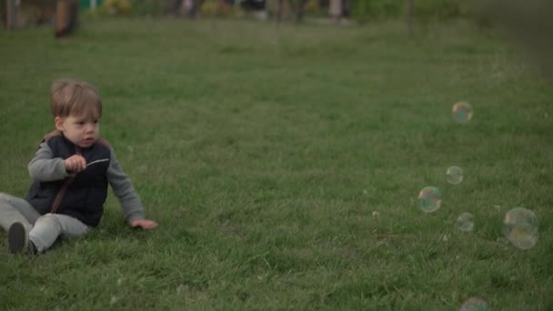 Маленькие дошкольные младшие братья и сестры дети ловят мыльные пузыри в весеннем парке на закате. Счастливые дети друзья весело проводят время. Свободное время природа. Семья, дружба, детство — стоковое видео