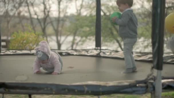 Vår, sport, høytid, familie, barndom, langsom bevegelse Tre glade små barn førskolebarn Barn leker morsomme hoppeballer på trampoline utenfor solnedgang i parken – stockvideo