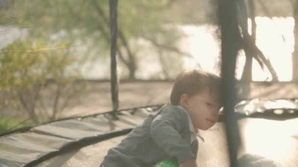 İlkbahar, spor, bayram, aile, çocukluk üç mutlu küçük çocuk anaokulu kardeş çocuklar trambolinde zıplayarak eğleniyorlar güneşli bir akşam günbatımında parkta. — Stok video