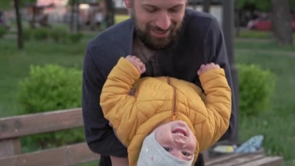 Menschen im Park. Papa hält die kleine Tochter auf dem Arm und kitzelt sie. Eltern und lustige Kinder, die im Freien spazieren gehen. Vatertag, glückliche Familie, Kindheit, Elternschaft — Stockvideo