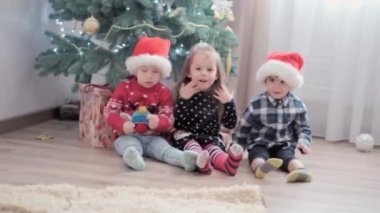 Üç otantik mutlu Joy çocuğu süslü Noel ağacının yanında oturup birlikte eğleniyorlar. Anaokulundaki küçük çocuklar evde yeni yılı kutluyorlar. Kış, tatil, aile kavramı
