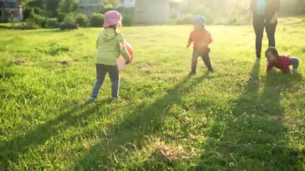 Літо, відпустка, природа, щаслива сім'я, дитинство, дружба - двоє маленьких дітей дошкільного віку мама мати дитина діти брати і сестри близнюки бігають грати весело з м'ячем у парку на траві на заході сонця — стокове відео