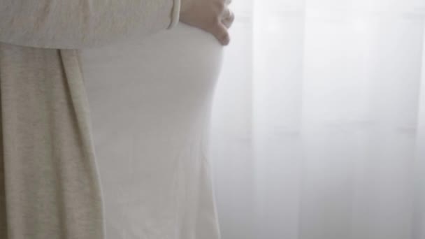 Hiteles aranyos terhes nő érzi magát boldog otthon vigyáz a gyermekre. A fiatal várandós anya a hasában tartja a babát az ablak mellett. Terhesség, terhesség, anyaság, életmód — Stock videók