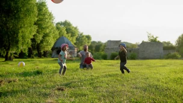 Лето, каникулы, природа, счастливая семья, детство, отцовство, день отца - папа с маленькими детьми дошкольного возраста бегают весело играть с большим надувным мячом в парке на закате снаружи — стоковое видео