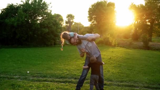Summer, vacation, nature, happy family, childhood, paternity, father Day - Dad with small preschool children baby kids playing plane spread arms wings have fun sit on shoulder in park meadow at sunset — Stock Video