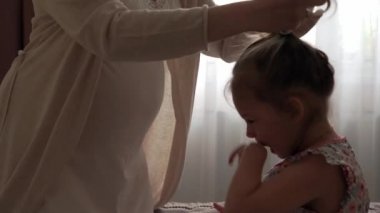 Hamile bir kadın çocuğuna baktığı için kendini mutlu hissediyor. Müstakbel anne, küçük kızıyla karnını okşuyor ve göbeğini öpüyor. Doğum öncesi bakım, hamilelik, annelik kavramı..