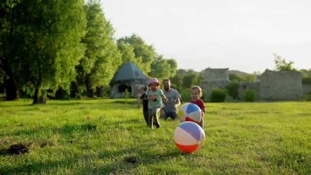 Verano, vacaciones, naturaleza, familia feliz, infancia, paternidad, día del padre papá con los niños pequeños del niño preescolar corren divertirse jugando con la bola inflable grande en el parque al atardecer afuera — Vídeos de Stock