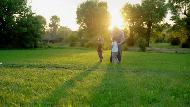 Lato, wakacje, przyroda, szczęśliwa rodzina, dzieciństwo, ojcostwo, Dzień Ojca - Tata z małymi przedszkolakami dzieci biegają bawić się usiąść na ramionach z dużą nadmuchiwaną piłką w parku o zachodzie słońca — Wideo stockowe