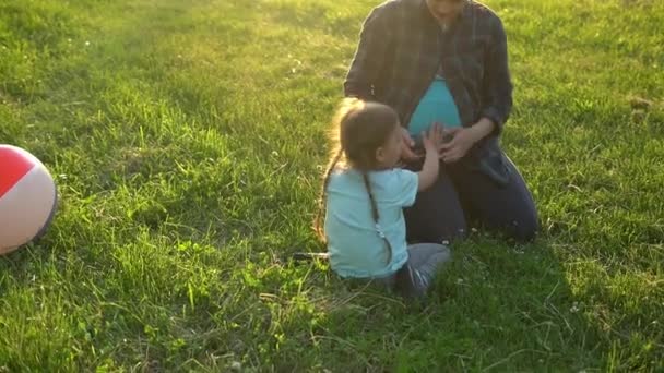 Summer, nature, happy family, pregnancy - young pregnant woman mother with two small toddler children sit on grass in park at sunset. Kids stroking mom belly kiss have fun, laugh spend time together — Stock Video