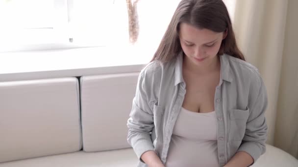 Auténtica mujer embarazada linda con pop se siente feliz en casa con el vientre. Joven madre jugar hoyuelo simple en el sofá blanco cerca de la ventana. Atención prenatal de maternidad, embarazo, maternidad, concepto de estilo de vida — Vídeos de Stock