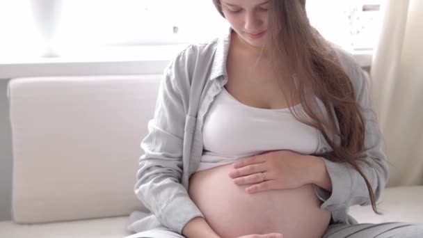 Gros plan heureuse femme enceinte touchant son ventre dans son lit à la maison. mère attentionnée caresse ventre nu gros ventre avec les mains sur la pièce lumineuse dans la journée ensoleillée d'été. grossesse, maternité, personnes, attente — Video