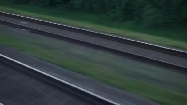 View from window of speed train with glare on glass and parallel rails on landscape of meadows and forest before sunset in summer background. Transport, travel, road, railway, comnication concept — Stock Video