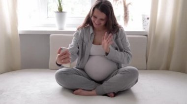 Tabletli mutlu hamile bir kadın, cep telefonuyla arkadaşlarıyla sohbet ederek kocasıyla akıllı telefonlardan iletişim kuruyor. gebelik, teknoloji, tıp