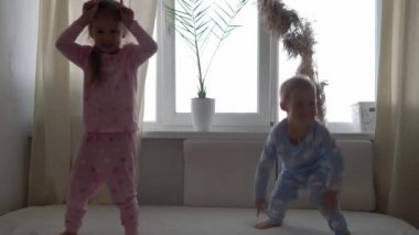 İki gülümseyen preshool, yeni yürümeye başlayan çocuk beyaz yatakta pijamalarıyla uzanan kız ve erkek çocuk. Kardeş ikizler evde karantinada eğleniyor, mutlu çocuklar. Arkadaşlık, aile, eğitim kavramı