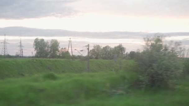 Vue de fenêtre de train de vitesse avec éblouissement sur verre et rails parallèles sur le paysage des prairies et de la forêt avant le coucher du soleil en arrière-plan d'été. Transport, voyage, route, chemin de fer, concept de communication — Video