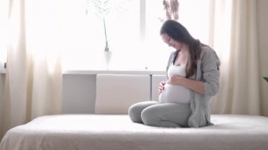 Hamilelik, annelik, insanlar, beklenti konsepti mutlu hamile bir kadın evde karnına dokunuyor şefkatli bir anne çıplak karnını okşuyor güneşli bir yaz gününde güneşli bir odada, elleriyle karnını okşuyor.