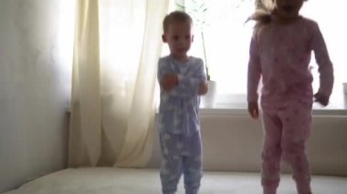 İki gülümseyen preshool, yeni yürümeye başlayan çocuk beyaz yatakta pijamalarıyla uzanan kız ve erkek çocuk. Kardeş ikizler evde karantinada eğleniyor, mutlu çocuklar. Arkadaşlık, aile, eğitim kavramı
