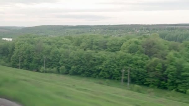 Vy från fönstret av snabbtåg med bländning på glas och parallella skenor på landskapet av ängar och skog före solnedgången i sommar bakgrund. Transport, resor, väg, järnväg, kompositionskoncept — Stockvideo