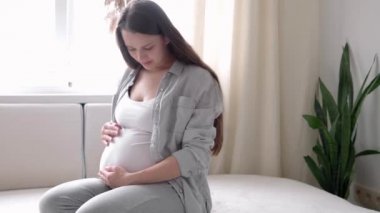 Hamilelik, annelik, insanlar, beklenti konsepti mutlu hamile bir kadın evde karnına dokunuyor şefkatli bir anne çıplak karnını okşuyor güneşli bir yaz gününde güneşli bir odada, elleriyle karnını okşuyor.