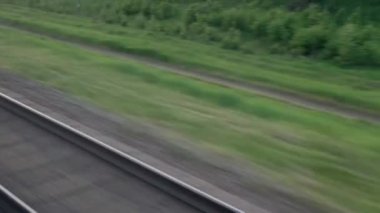 Hızlı trenin camında parlayan ışık ve yaz arkaplanındaki günbatımından önce çayırların ve ormanın manzarasında paralel raylar. Ulaşım, seyahat, yol, demiryolu, zina kavramı