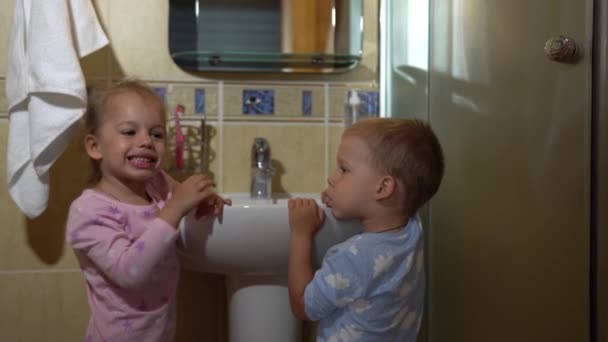 Retrato feliz lindo joven preescolar simulacros niños niño y niña cepillarse los dientes en el baño y sonreír. Rutina diaria de salud infantil. Los niños caucásicos se lavan mirando el espejo en casa. Estilo de vida — Vídeos de Stock