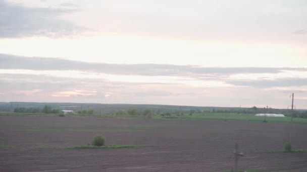 Widok z okna pociągu dużych prędkości na krajobraz pięknej przyrody pole wiejskie domy i las na wieczór zmierzch niebo zachód słońca w tle lata. Transport, podróże, kolej, koncepcja komunikacji — Wideo stockowe