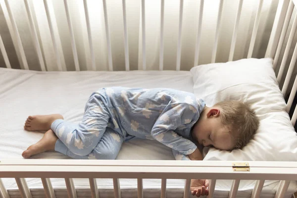 Вид сверху Милый маленький 2-3 лет дошкольный мальчик малыш спит сладко в белой кроватке во время обеденного отдыха в голубой пижаме с подушкой дома. Детство, отдых, комфорт, медицина, концепция здоровья — стоковое фото
