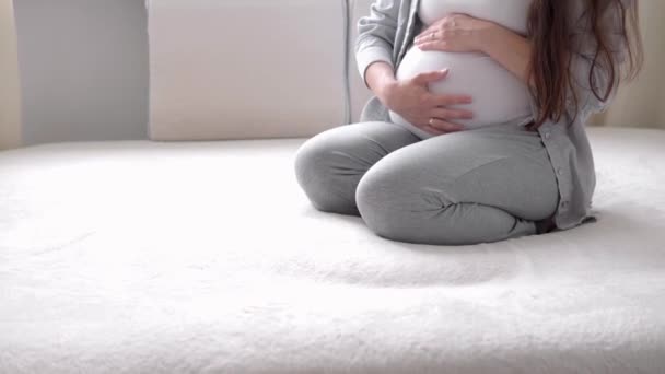 Gravidez, maternidade, pessoas, conceito de expectativa - mulher grávida feliz tocando sua barriga na cama em casa cuidar mãe acaricia grande barriga nua com as mãos, na sala de luz no dia ensolarado de verão — Vídeo de Stock