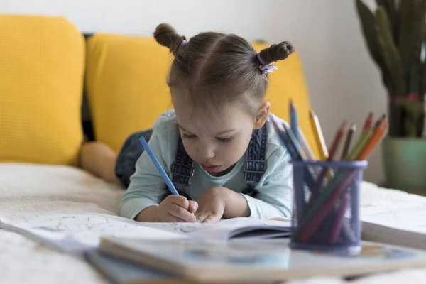 Schick lächelnd zeichnen Kleinkinder mit Bleistiften, die ihnen auf dem Bauch im gelben Bett liegen. kleine süße Leser haben Spaß, glückliches Kind in Quarantäne zu Hause. Freundschaft, Familie, Bildung — Stockfoto