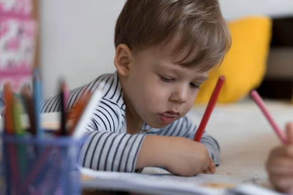 Schick lächelnd zeichnen Kleinkinder mit Bleistiften, die ihnen auf dem Bauch im gelben Bett liegen. kleine süße Leser haben Spaß, glückliches Kind in Quarantäne zu Hause. Freundschaft, Familie, Bildung — Stockfoto