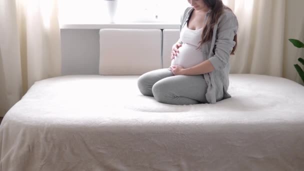 Graviditet, moderskap, människor, förväntan koncept - lycklig gravid kvinna vidrör magen i sängen hemma vårdande mor stroke naken stor mage med händer, på ljusa rum i solig sommardag — Stockvideo