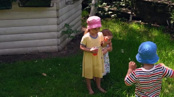 Güzel anaokulu şakaları. Çocuklar ve kızlar sıcak yaz aylarında sabun köpüğü üflüyor. Bahçede oynayan çocuklar. Parkta bebek ya da açık havada güneşli bir günde bahçe. Çocukluk, Meslek, Ebeveynlik, Aile kavramı — Stok video
