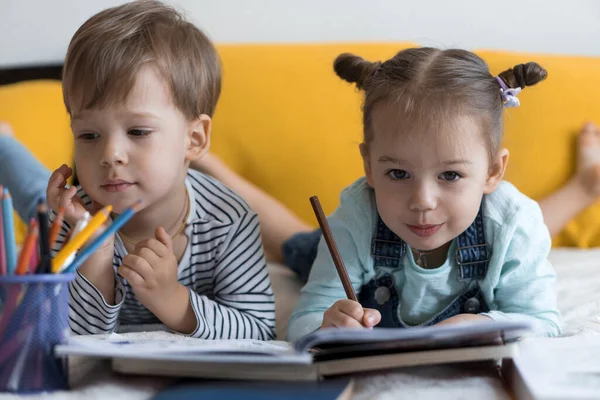 Zeki, gülümseyen, küçük bir çocuk çocuk ve kız sarı yatakta göbeklerinde kalemlerle resim yapıyorlar. Küçük sevimli okuyucu evde karantinada eğleniyor, mutlu çocuk. Arkadaşlık, aile, eğitim.