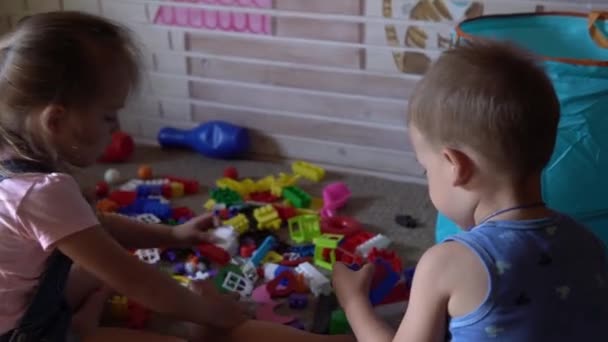 Pequeños hermanos preescolares niños sentados en el suelo con juguetes en la habitación de los niños. chicos están jugando con constructor en la sala de juegos. los niños han pasado un rato divertido en casa. Infancia, amistad, concepto de desarrollo — Vídeos de Stock