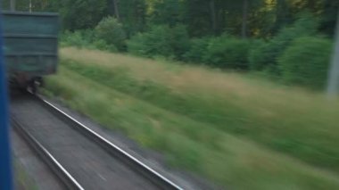 Pencereden yüksek hızlı tren manzarası güzel doğa manzarası vahşi arazi ve orman rayları yaz arkaplanında akşam günbatımında tren rayları. Ulaşım, seyahat, demiryolu, iletişim konsepti